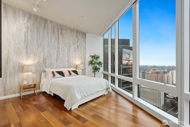 bedroom with wood-type flooring, rail lighting, and floor to ceiling windows