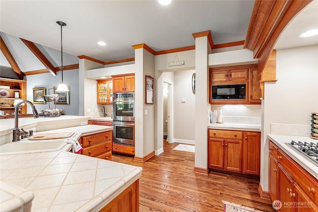 kitchen with wood finished floors, double oven, black microwave, pendant lighting, and a sink