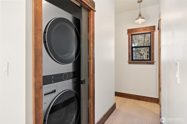 clothes washing area with stacked washer and dryer, baseboards, laundry area, and light wood-style floors