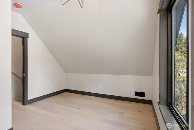 additional living space featuring light wood-type flooring, baseboards, visible vents, and lofted ceiling