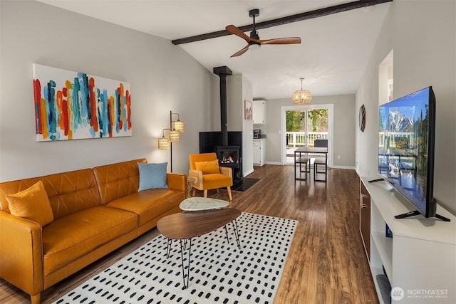 living room with wood finished floors, baseboards, lofted ceiling with beams, a wood stove, and ceiling fan with notable chandelier