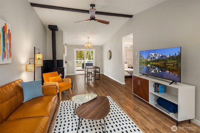 living area featuring vaulted ceiling with beams, baseboards, a wood stove, wood finished floors, and a ceiling fan