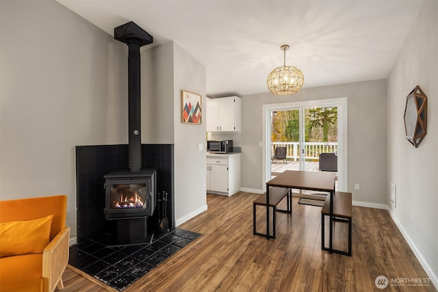 dining area featuring a wood stove, a notable chandelier, baseboards, and dark wood-style flooring