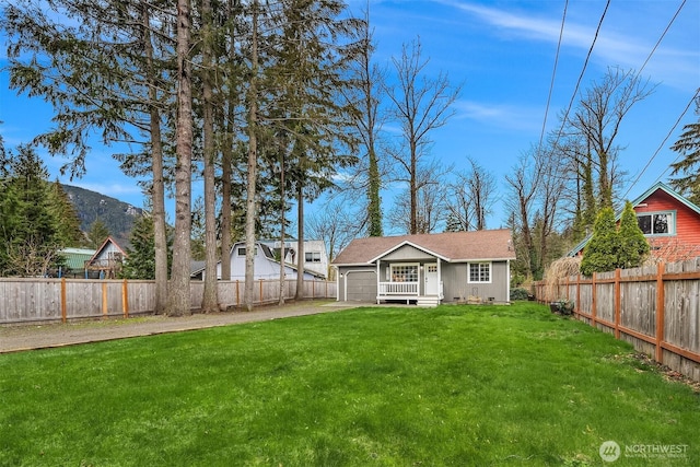 rear view of property with a lawn, a garage, driveway, and fence private yard