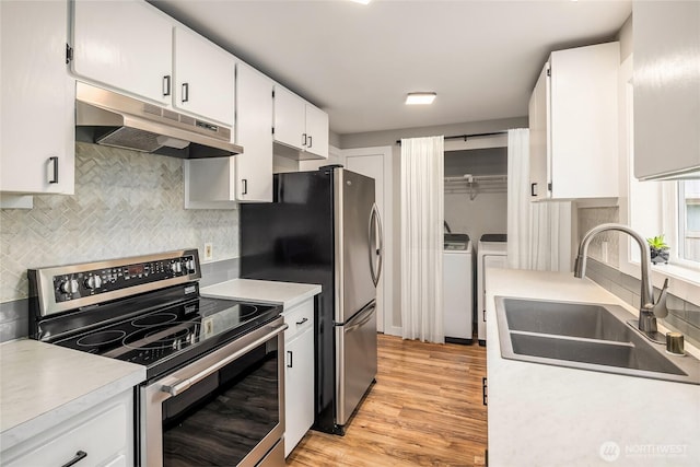 kitchen featuring light wood finished floors, washing machine and clothes dryer, a sink, stainless steel appliances, and under cabinet range hood