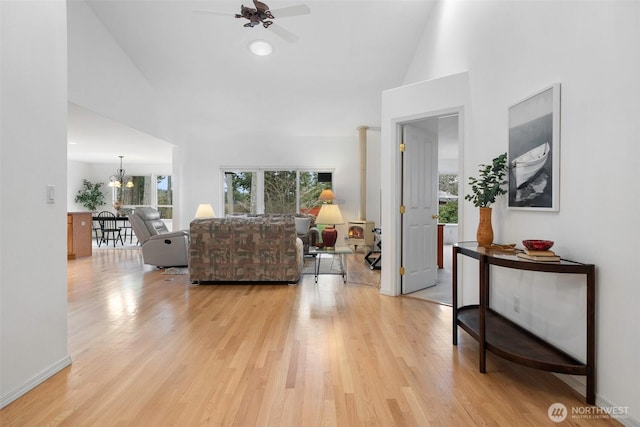 living area with light wood finished floors, ceiling fan with notable chandelier, baseboards, and a towering ceiling