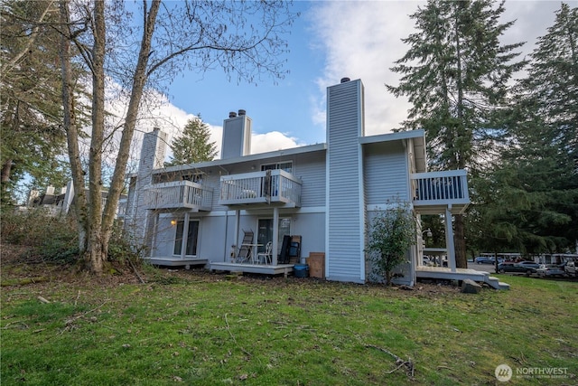 back of house featuring a yard, a chimney, and a balcony