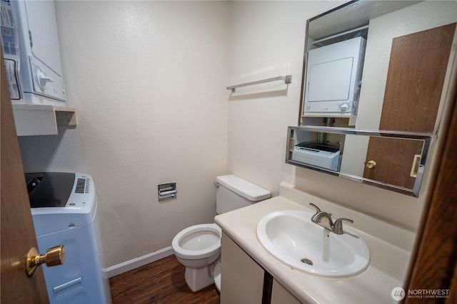 bathroom with toilet, wood finished floors, vanity, baseboards, and stacked washing maching and dryer