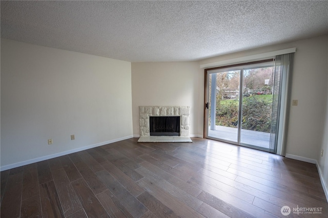 unfurnished living room with a textured ceiling, a stone fireplace, dark wood-style flooring, and baseboards