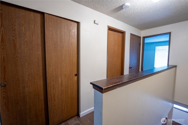 corridor featuring dark wood finished floors, a textured ceiling, and baseboards