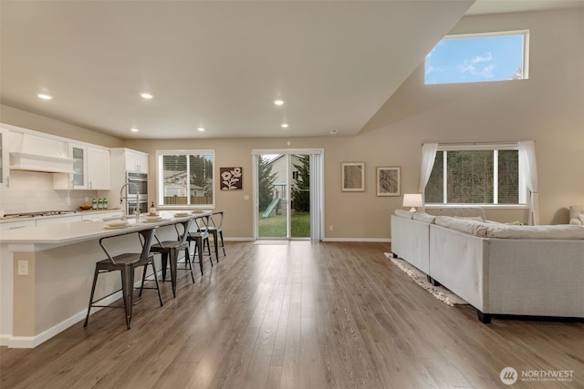 kitchen with light wood-type flooring, backsplash, gas stovetop, white cabinets, and a breakfast bar area