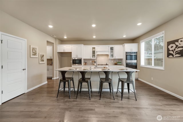 kitchen with white cabinetry, double oven, a breakfast bar, and a spacious island