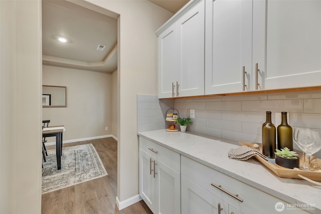 bar featuring light hardwood / wood-style flooring, white cabinetry, light stone countertops, and backsplash