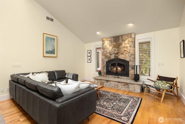 living room with light hardwood / wood-style flooring, a stone fireplace, and high vaulted ceiling