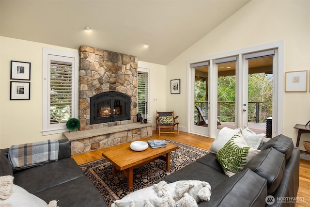 living room with hardwood / wood-style flooring, a stone fireplace, and vaulted ceiling