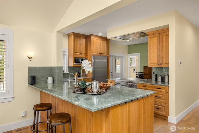 kitchen featuring built in appliances, a kitchen bar, light stone counters, kitchen peninsula, and tasteful backsplash