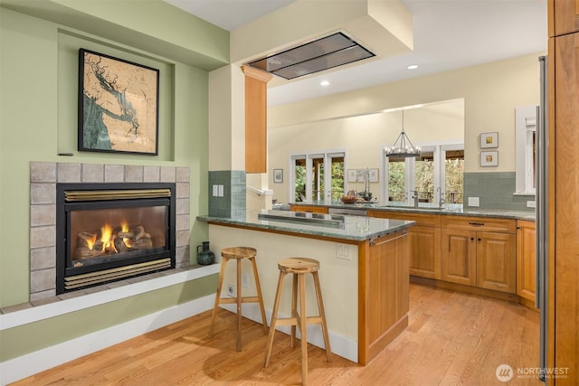 kitchen with light hardwood / wood-style flooring, stone counters, kitchen peninsula, a breakfast bar area, and decorative backsplash