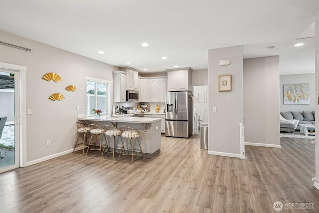 kitchen featuring stainless steel appliances, a peninsula, white cabinetry, a kitchen breakfast bar, and light wood-type flooring