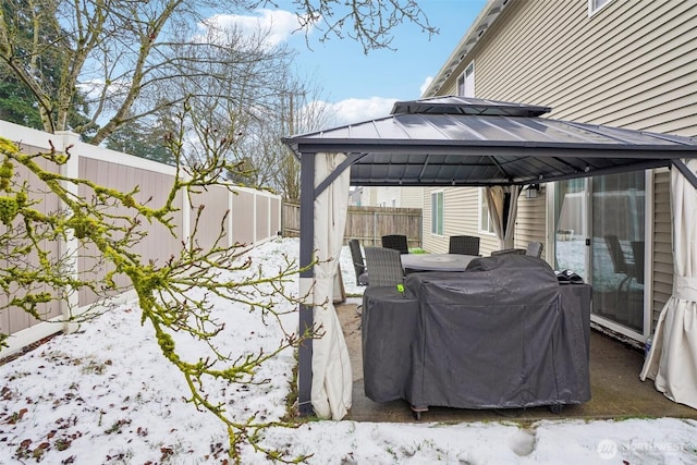 snow covered patio with outdoor dining space, a fenced backyard, and a gazebo