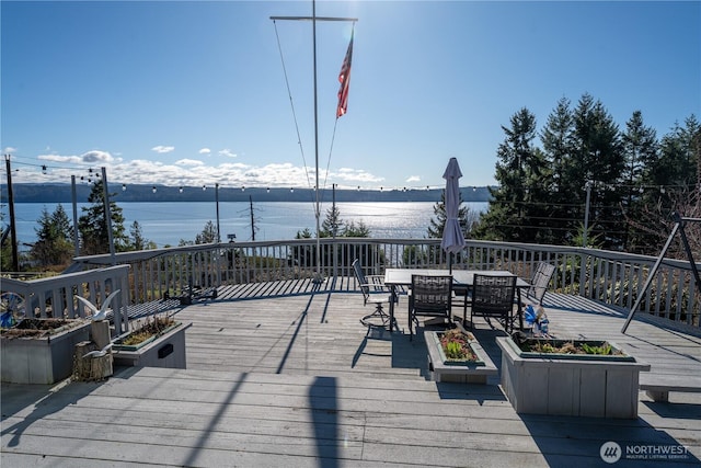 deck with outdoor dining area and a water view