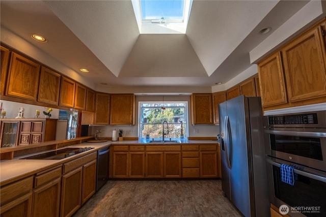 kitchen with a tray ceiling, a sink, light countertops, appliances with stainless steel finishes, and brown cabinets