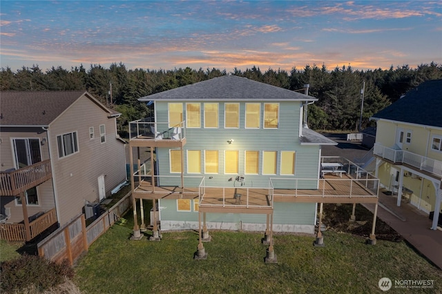 back house at dusk featuring a balcony and a lawn