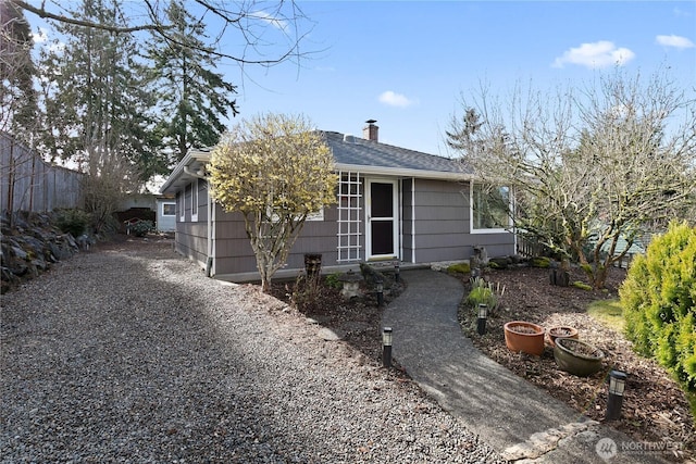 view of front facade featuring roof with shingles, a chimney, gravel driveway, and fence