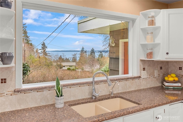 kitchen with a sink, dark stone counters, decorative backsplash, white cabinetry, and open shelves