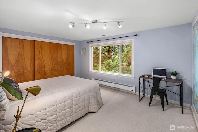 bedroom featuring a baseboard heating unit, baseboards, light colored carpet, and rail lighting