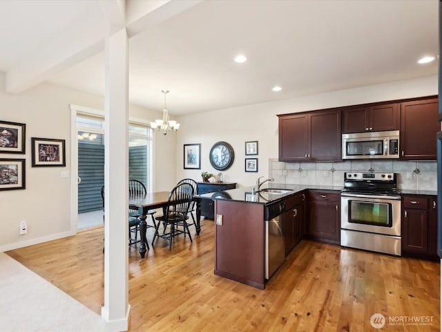 kitchen featuring stainless steel appliances, dark countertops, decorative light fixtures, and a peninsula