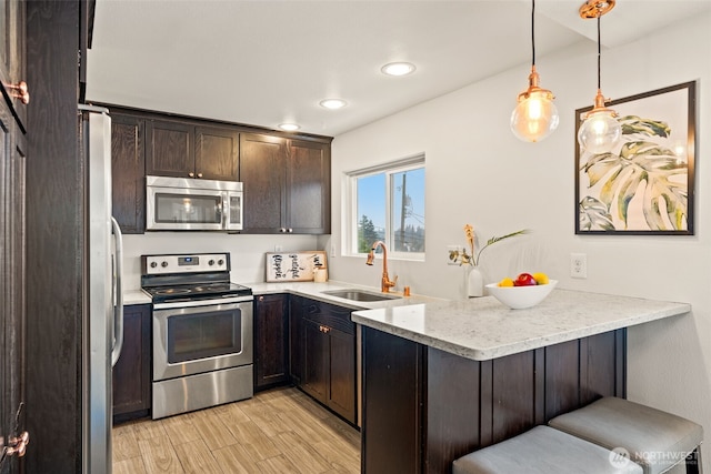 kitchen featuring kitchen peninsula, stainless steel appliances, decorative light fixtures, sink, and a breakfast bar area