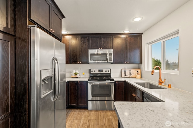 kitchen featuring light hardwood / wood-style flooring, dark brown cabinets, stainless steel appliances, light stone counters, and sink