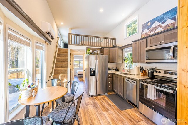 kitchen with stainless steel appliances, light wood-style flooring, an AC wall unit, a sink, and light stone countertops