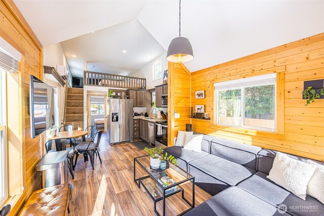 living room featuring high vaulted ceiling, light wood-type flooring, a healthy amount of sunlight, and stairs