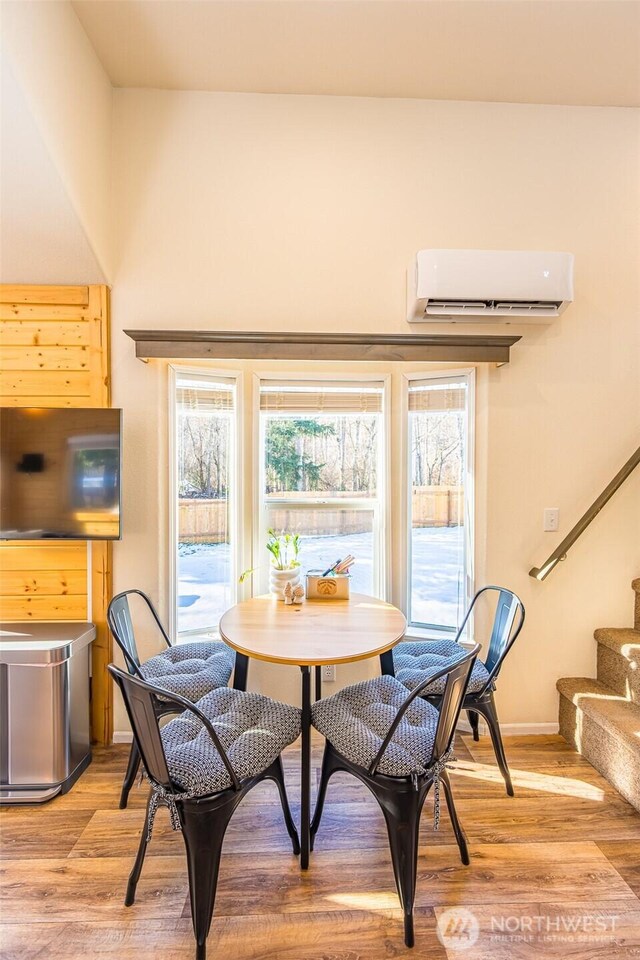 dining area featuring baseboards, a wall mounted air conditioner, light wood finished floors, and stairs