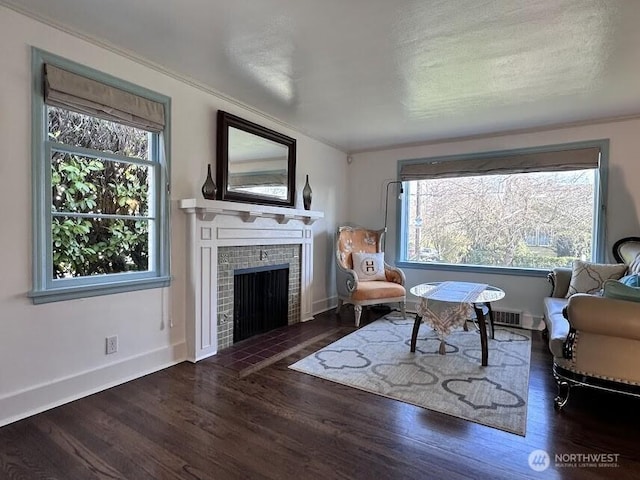 sitting room with a tiled fireplace, wood finished floors, and baseboards