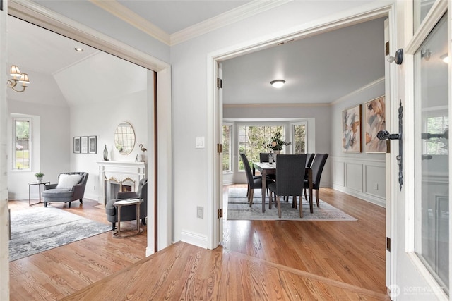 dining space with light wood-style flooring, a lit fireplace, crown molding, a decorative wall, and a notable chandelier