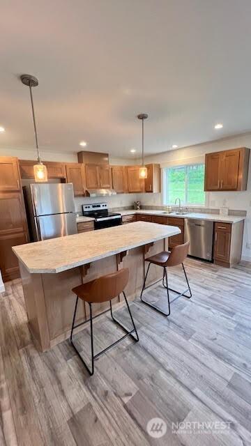 kitchen featuring a breakfast bar, a center island, hanging light fixtures, light wood-type flooring, and stainless steel appliances