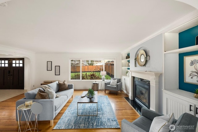 living area featuring crown molding, built in shelves, a premium fireplace, and light wood-style floors