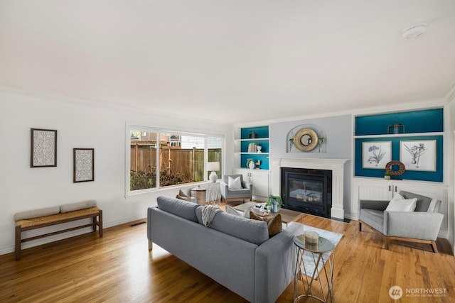 living area with ornamental molding, a glass covered fireplace, wood finished floors, and baseboards