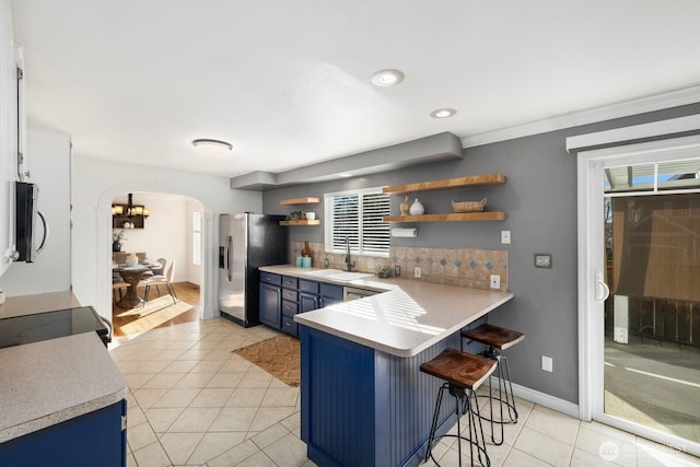 kitchen with arched walkways, stainless steel appliances, blue cabinetry, open shelves, and a kitchen bar