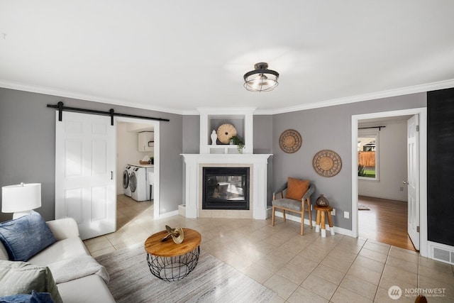 living area featuring washing machine and clothes dryer, a tiled fireplace, a barn door, ornamental molding, and light tile patterned flooring