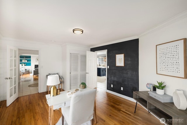 dining room featuring arched walkways, ornamental molding, wood finished floors, and baseboards