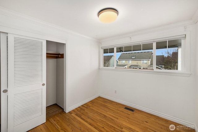 unfurnished bedroom featuring baseboards, visible vents, wood finished floors, crown molding, and a closet