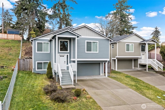 raised ranch featuring an attached garage, fence, driveway, board and batten siding, and a front yard