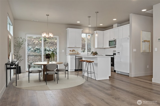 kitchen with light countertops, hanging light fixtures, appliances with stainless steel finishes, white cabinetry, and a kitchen island