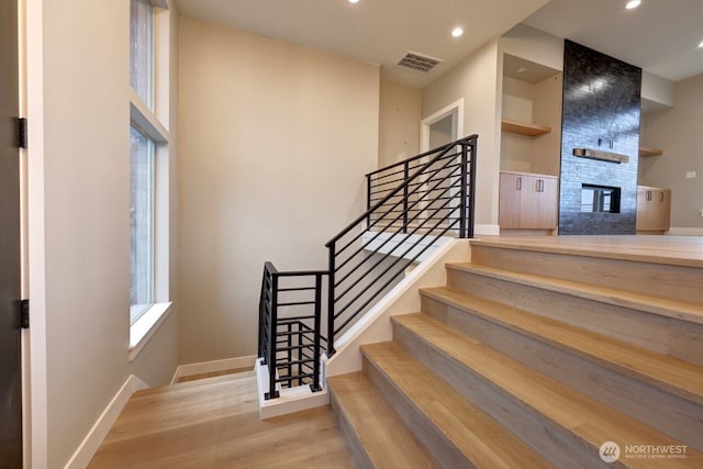 stairway with a large fireplace, wood-type flooring, and built in shelves