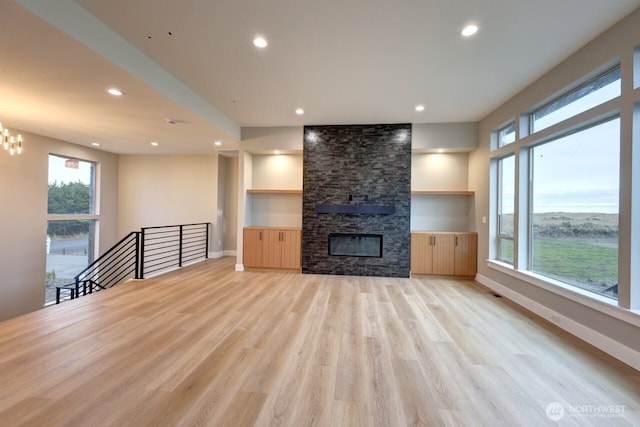 unfurnished living room with a fireplace, a notable chandelier, and light hardwood / wood-style flooring