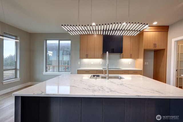 kitchen with hanging light fixtures, a healthy amount of sunlight, light stone counters, and decorative backsplash