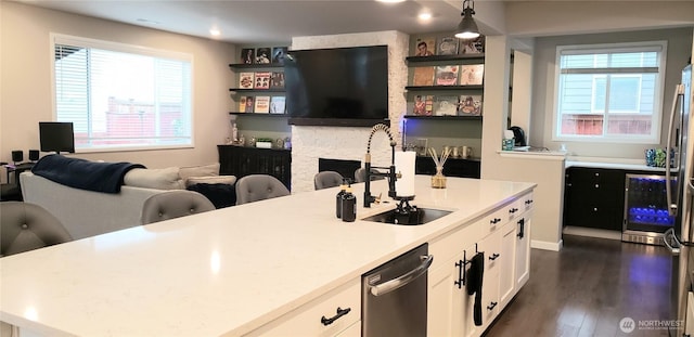 kitchen featuring decorative light fixtures, white cabinets, light countertops, dishwasher, and a center island with sink